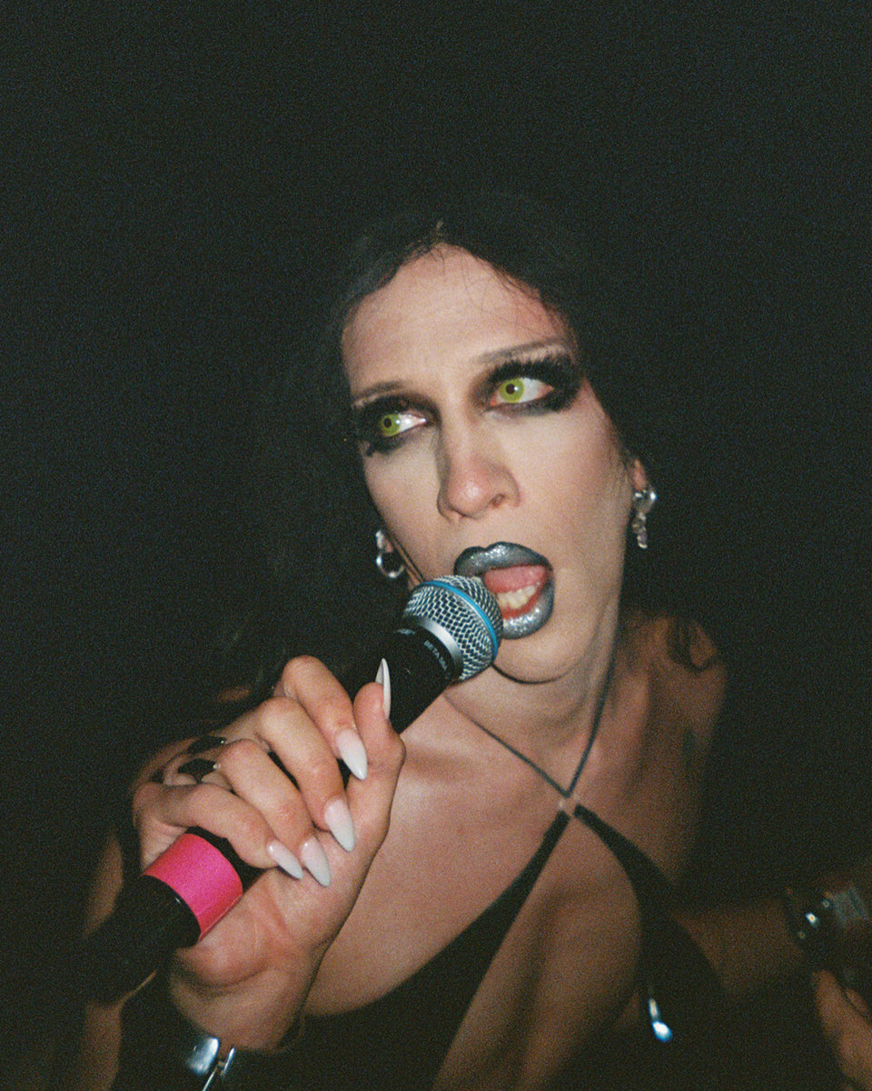Person with dramatic makeup holding a microphone against a dark background