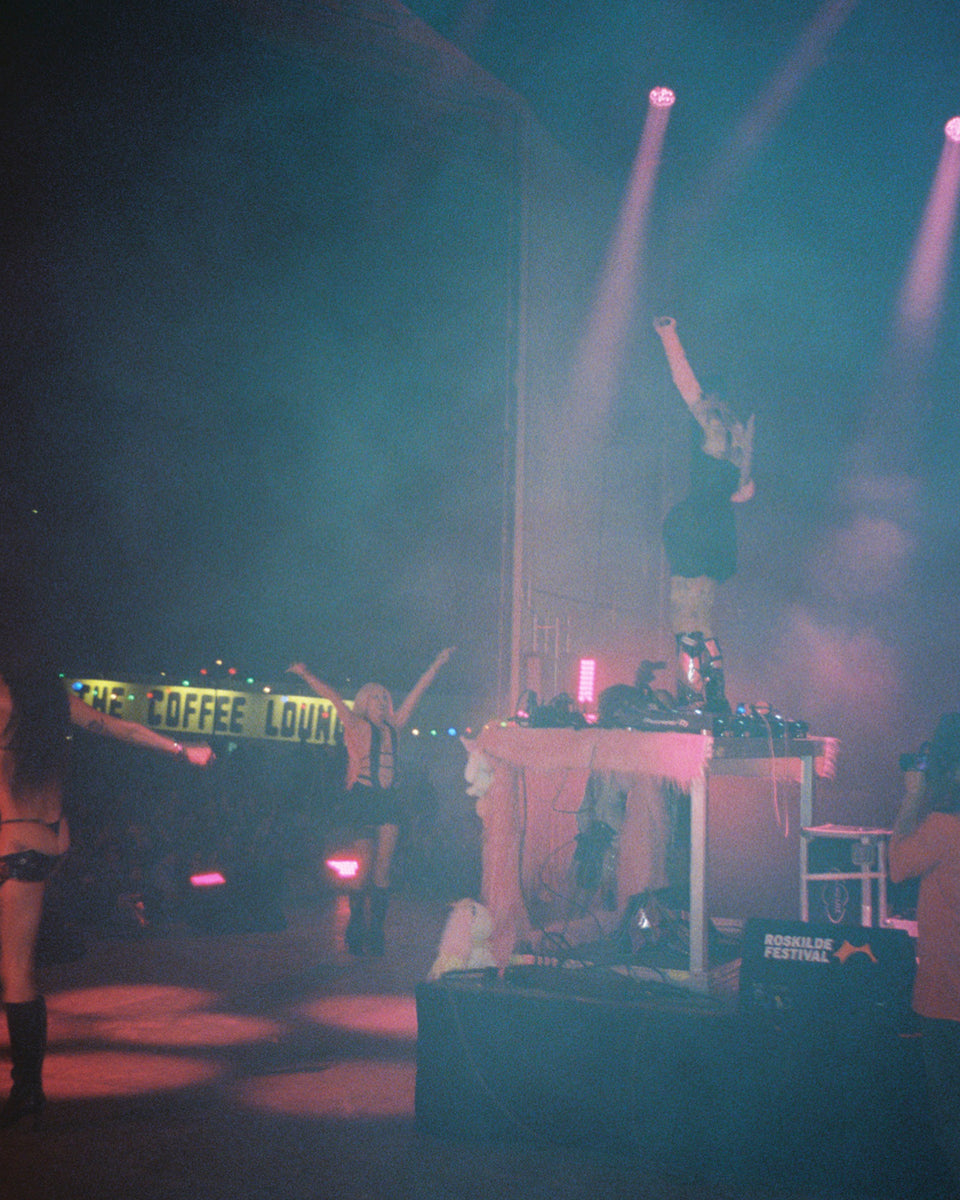 DJ set up on a stage with lights and a crowd in the background