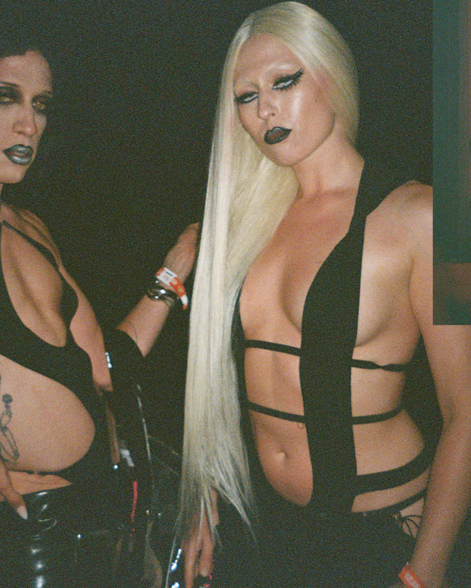Two women wearing black outfits with sheer panels against a dark background