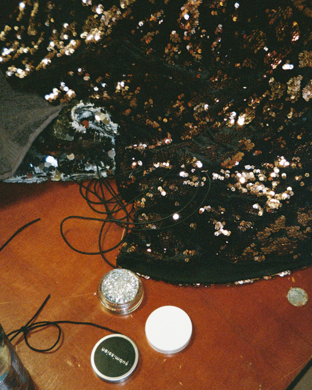 Black sequin fabric with silver submission beauty glitter on a brown surface, next to small containers.