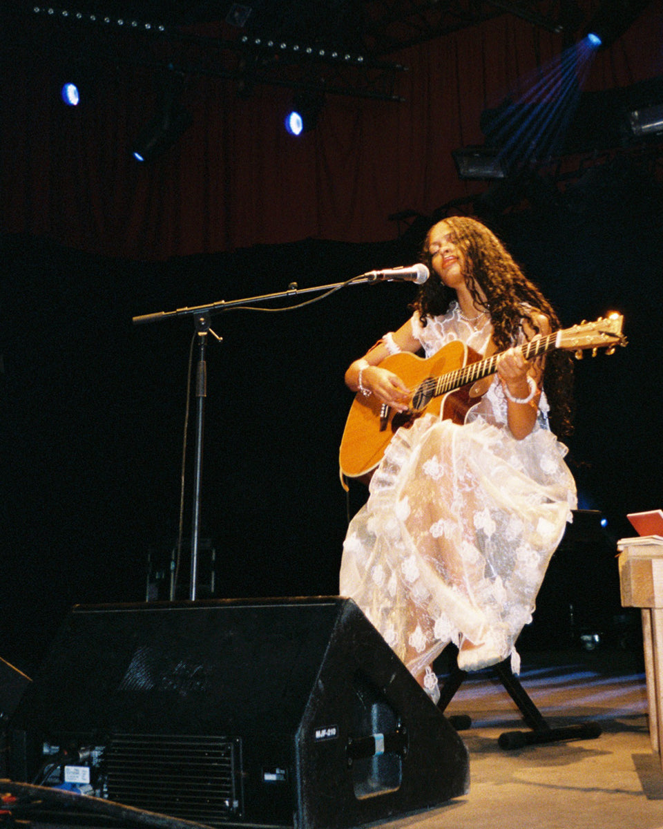Artist Annahstasia Enuke playing guitar on stage at Roskilde Festival with a microphone and dark background