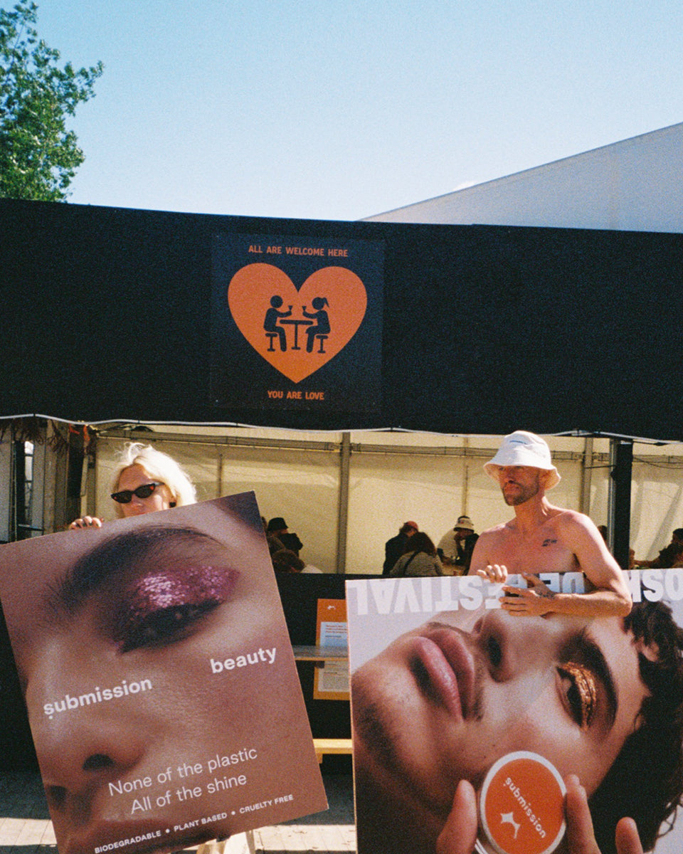 Outdoor event with people under a tent featuring a heart symbol and text, with promotional posters displayed.