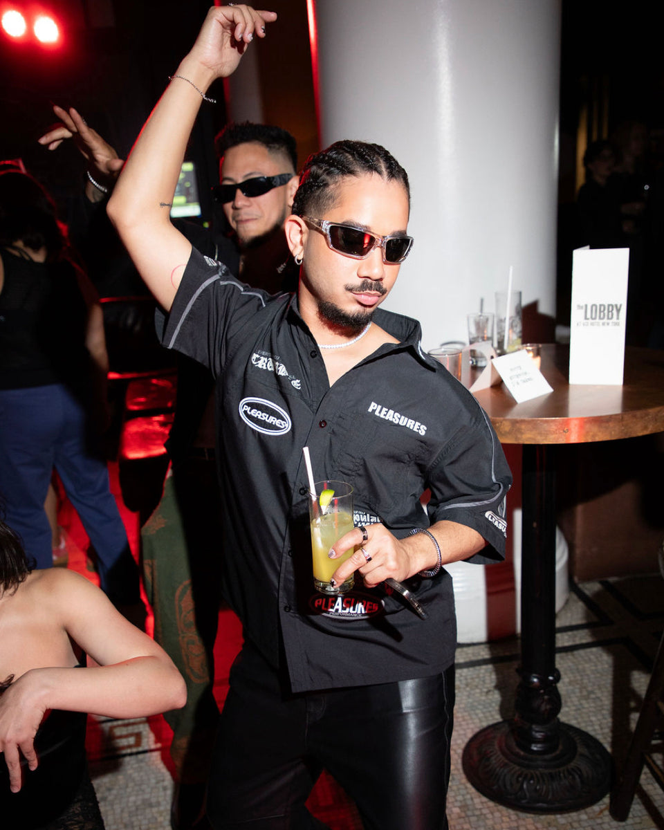 Man in a black shirt with sunglasses holding a drink at a party.