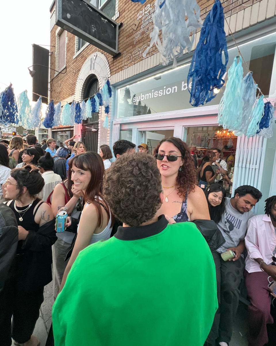 Crowd of people in a street setting with decorative elements and a store entrance.