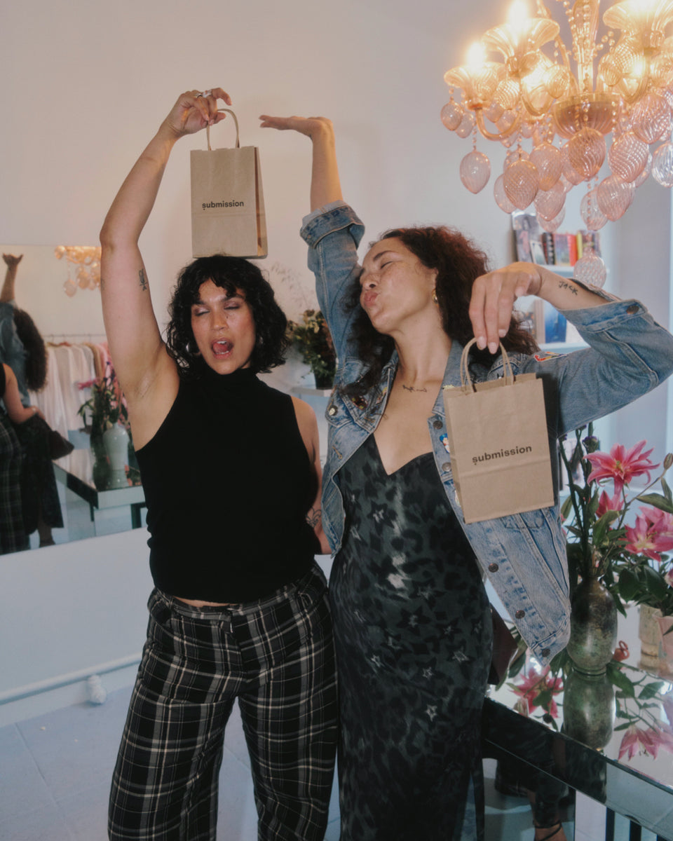 Two women holding brown paper bags in a room with decorative elements
