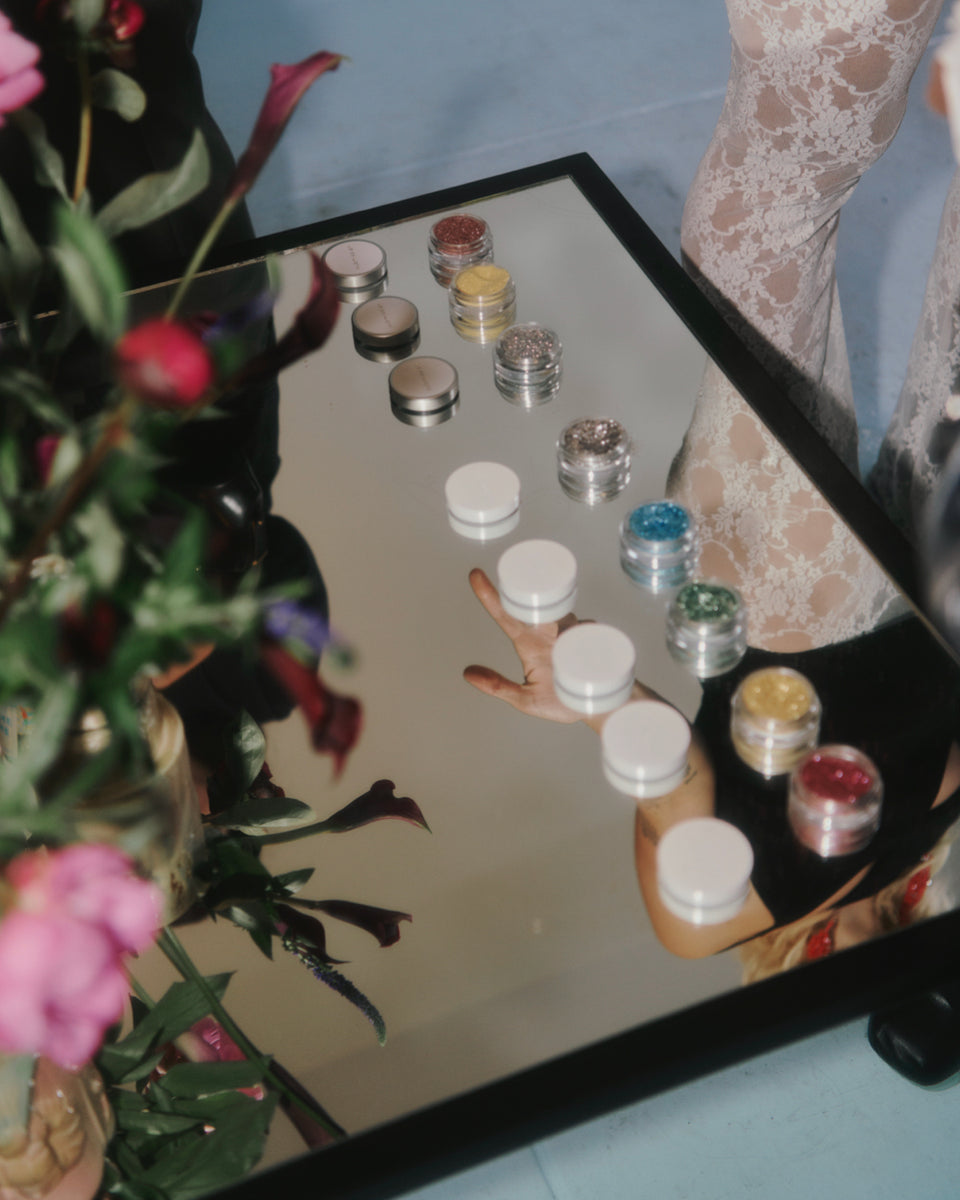 Makeup containers on a mirror with flowers in the foreground