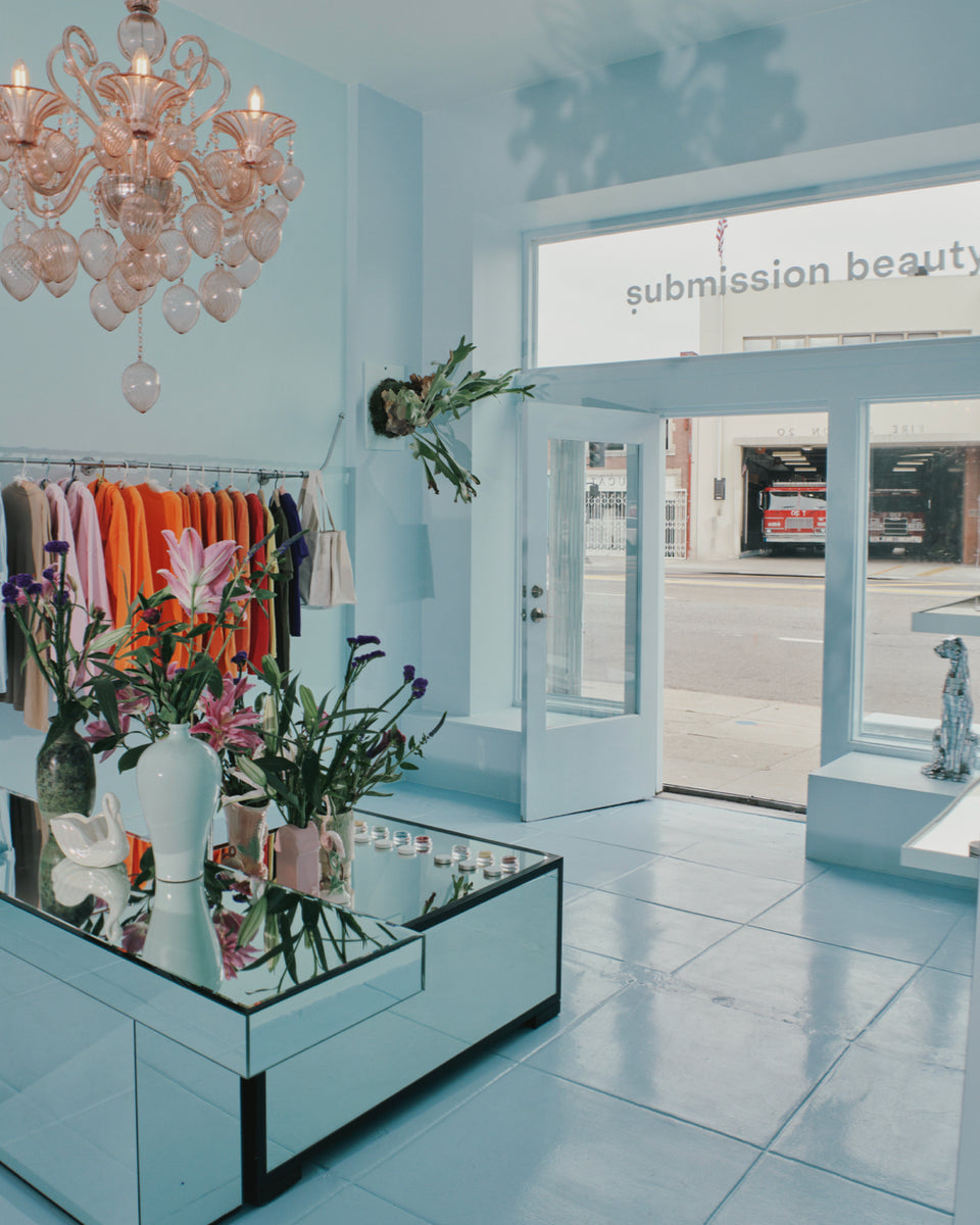 Interior of a stylish submission beauty store with light blue walls, floral arrangements, and a chandelier.