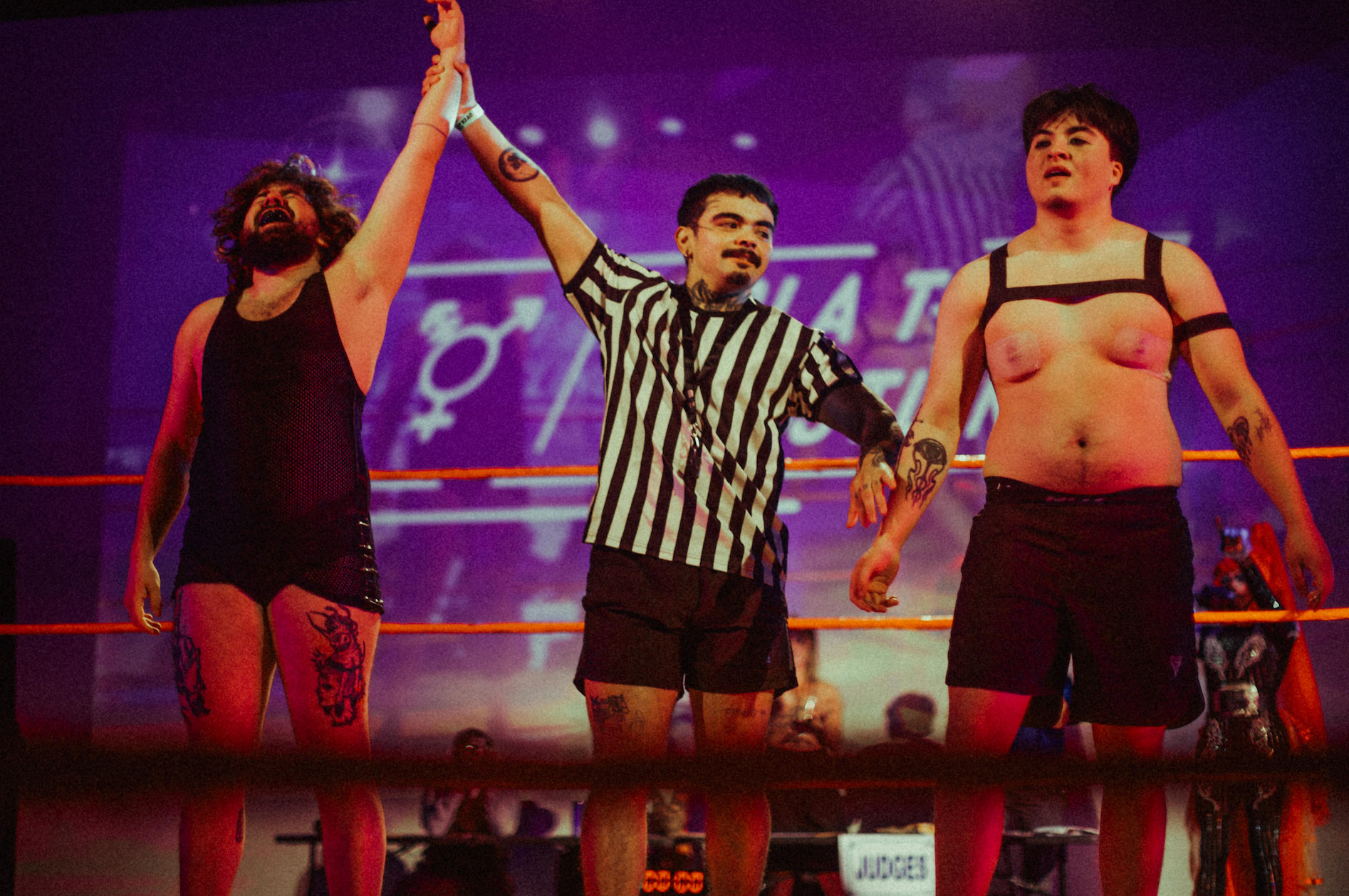 Three men in a wrestling ring with a referee, one on each side.