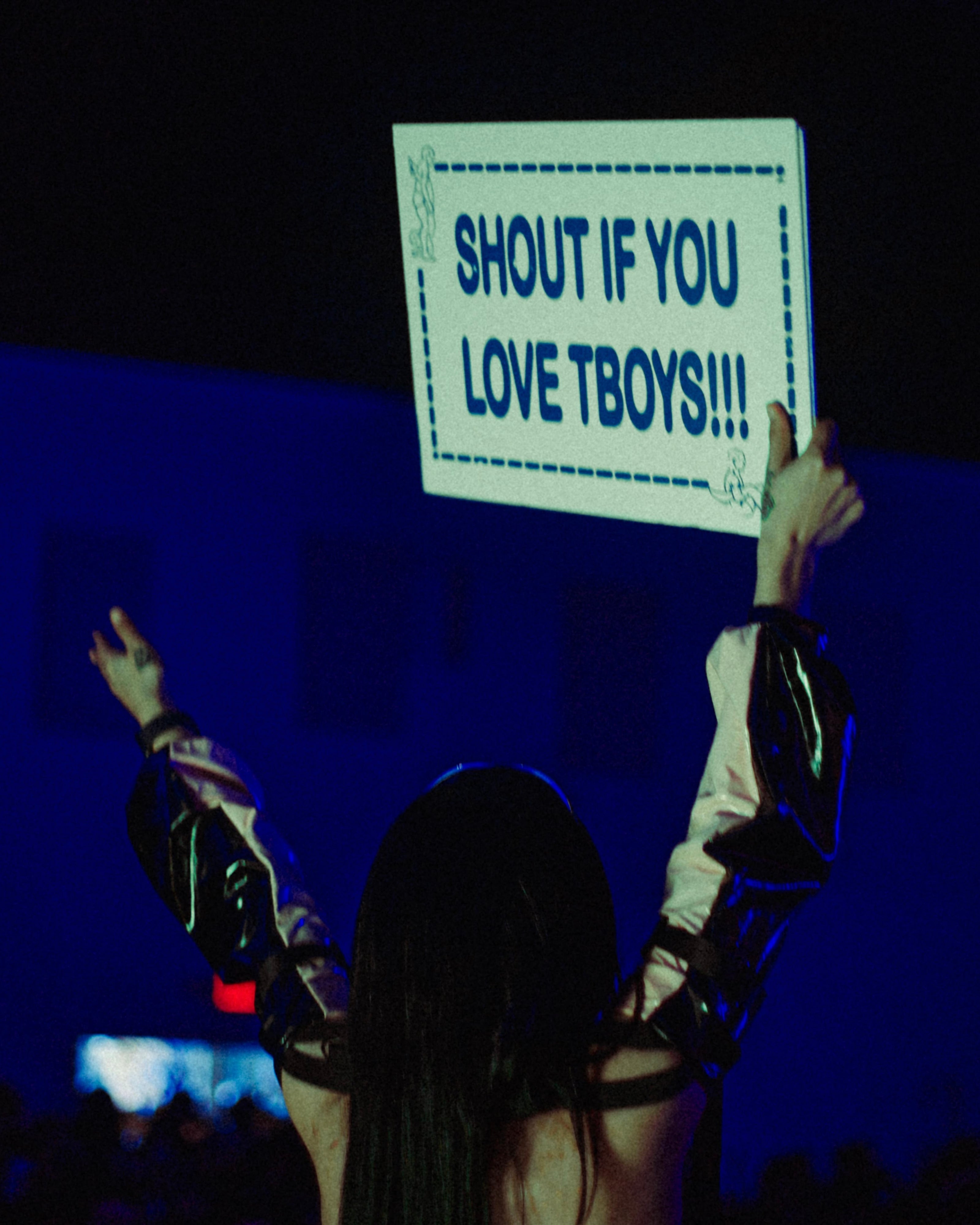 Person holding up a sign in a darkened room with blue lighting.