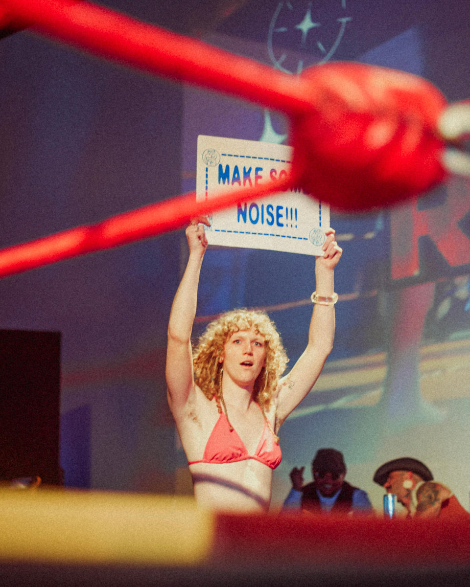Woman in bikini holding a sign in a boxing ring.