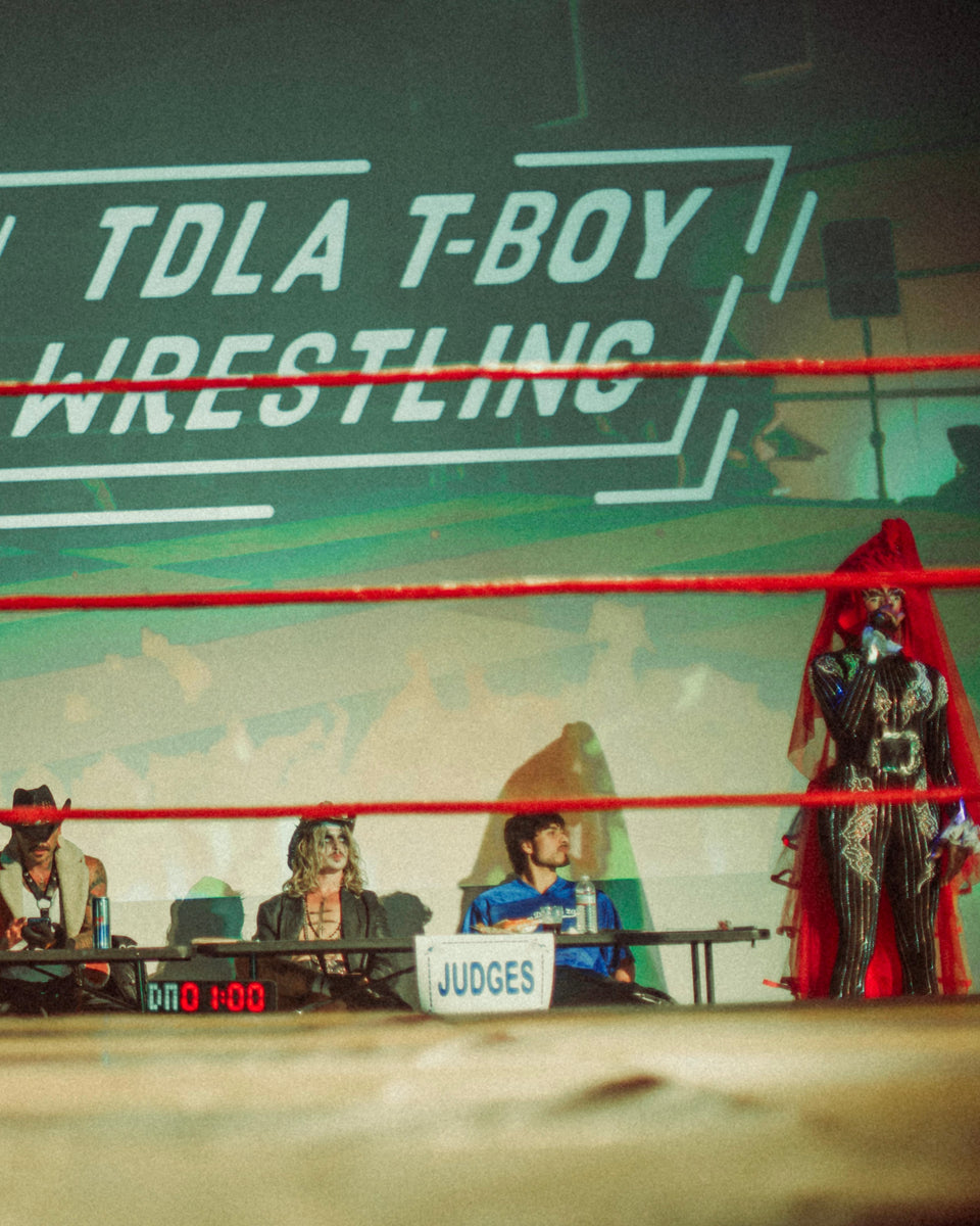 Wrestling event with judges and a wrestler in a red cape.