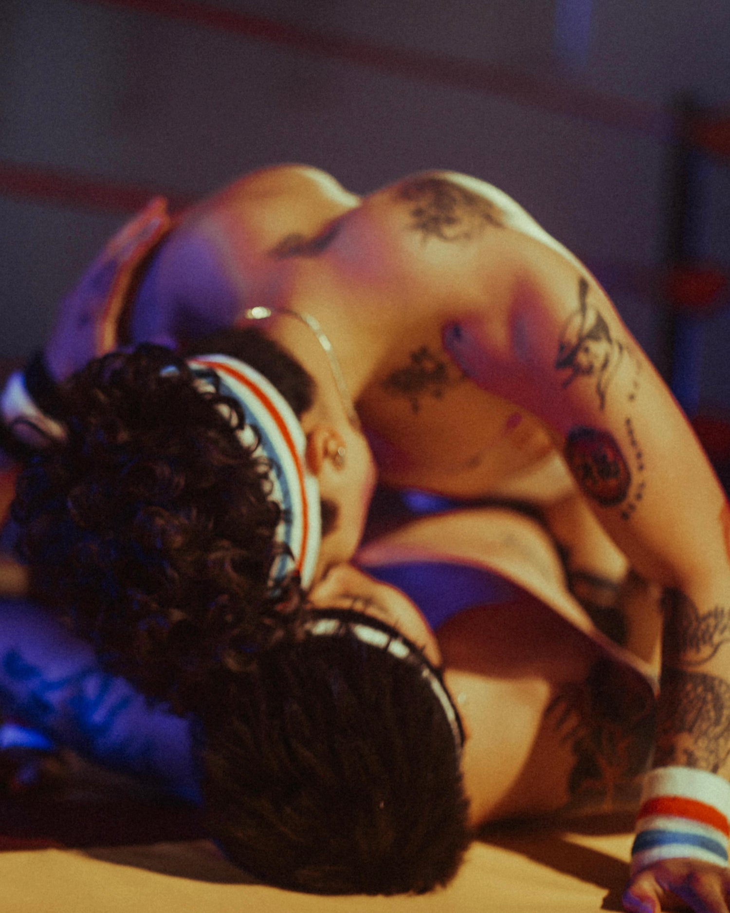 Person in a wrestling ring with another person on top, both wearing headgear.