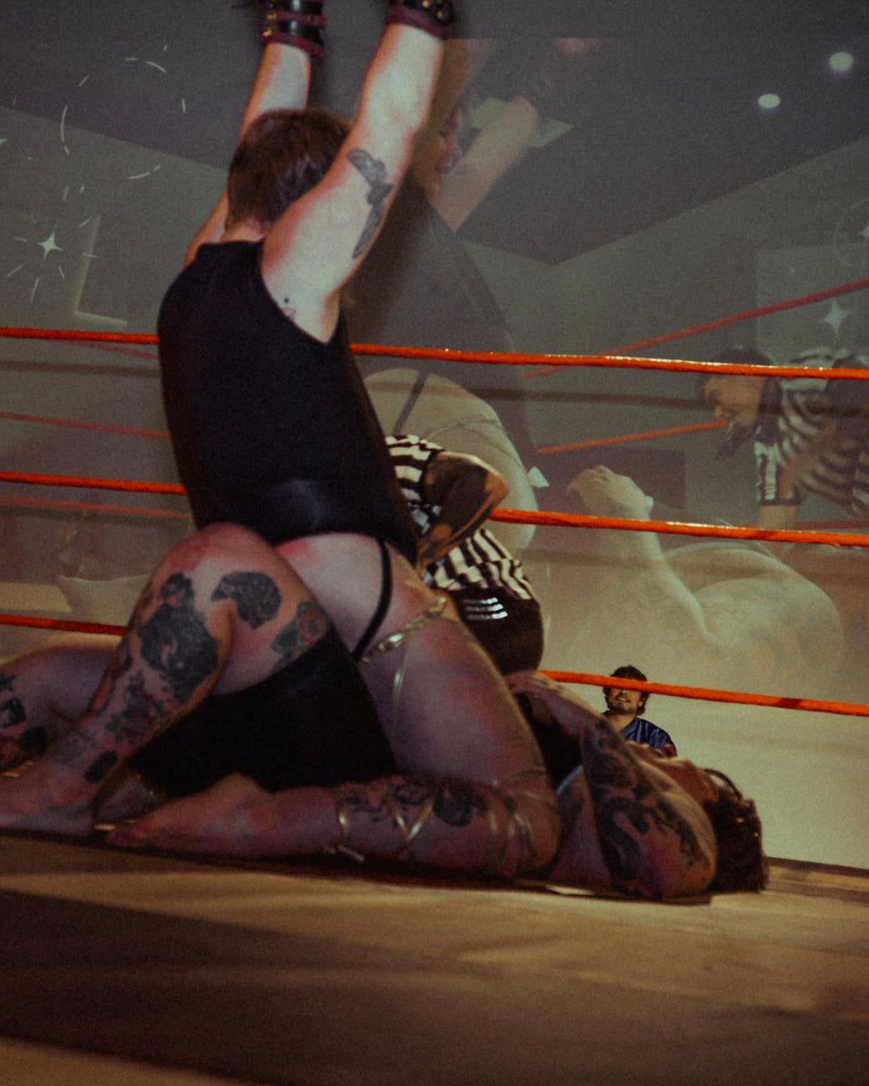 Person in black outfit with tattoos on arms and legs, lying on a boxing ring.