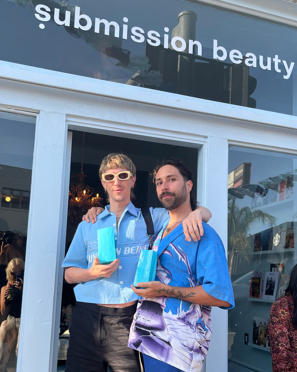 Two people holding blue products in front of a store named 'submission beauty'.