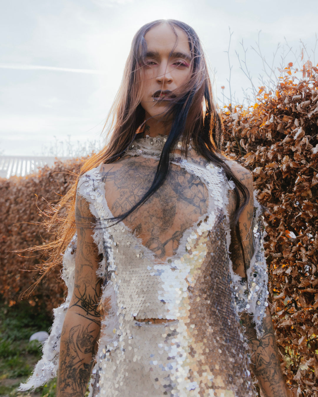djg2g with tattoos and sequined outfit standing outdoors with snow on their body.