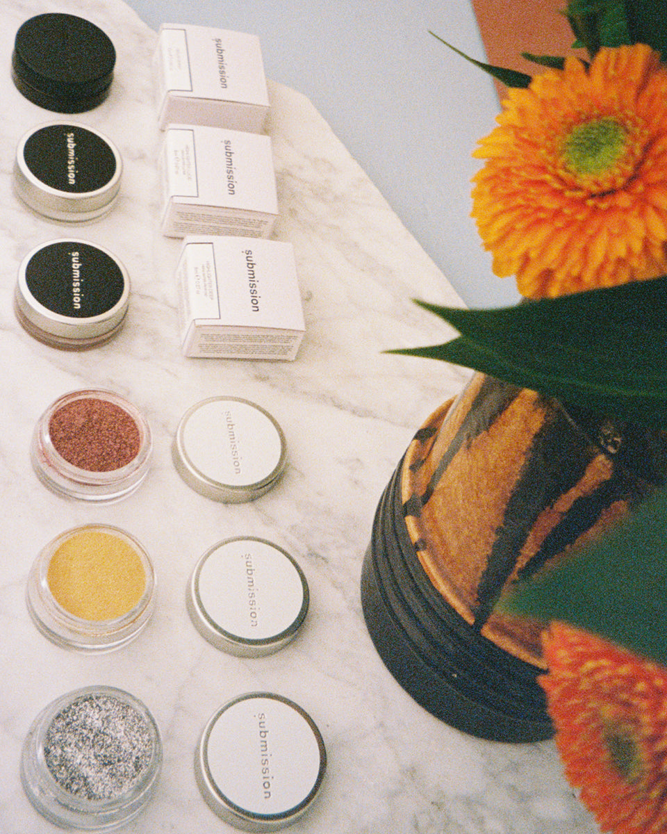 Submission Beauty plant based Makeup products including jars and boxes on a marble surface with flowers in the background
