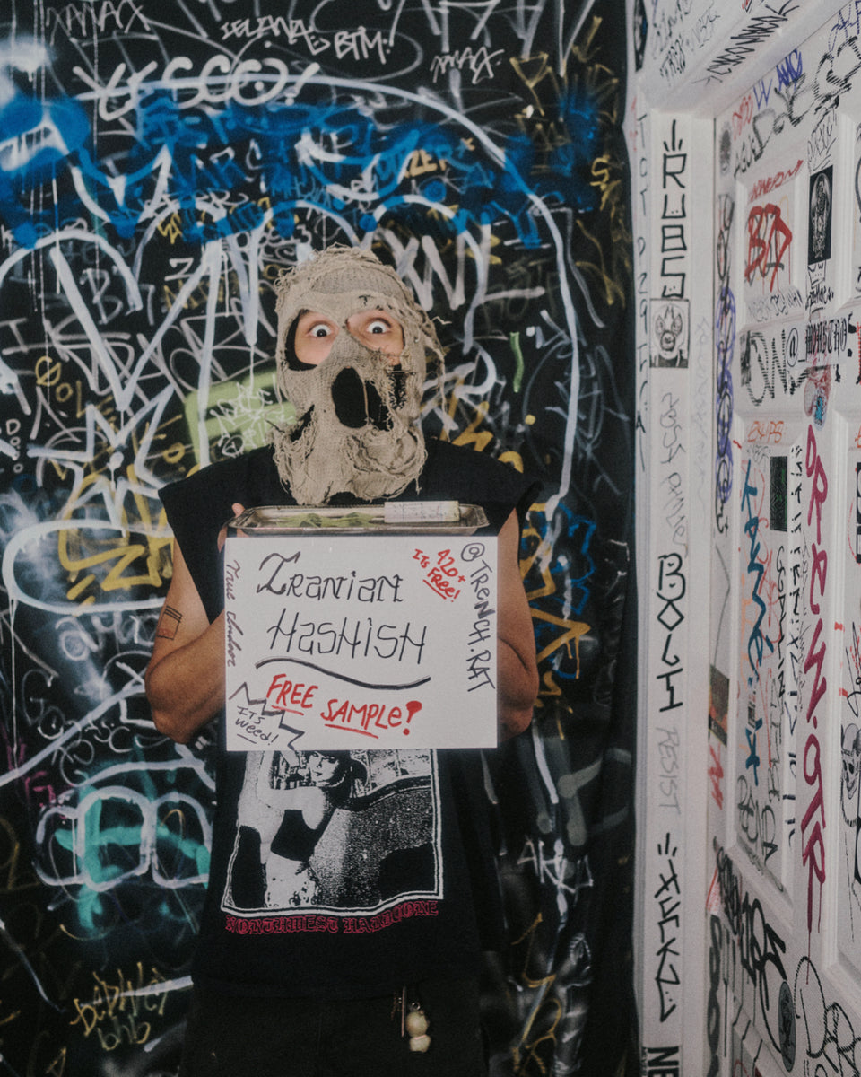 Stylized image of a person holding a sign with text in a graffiti-covered room.
