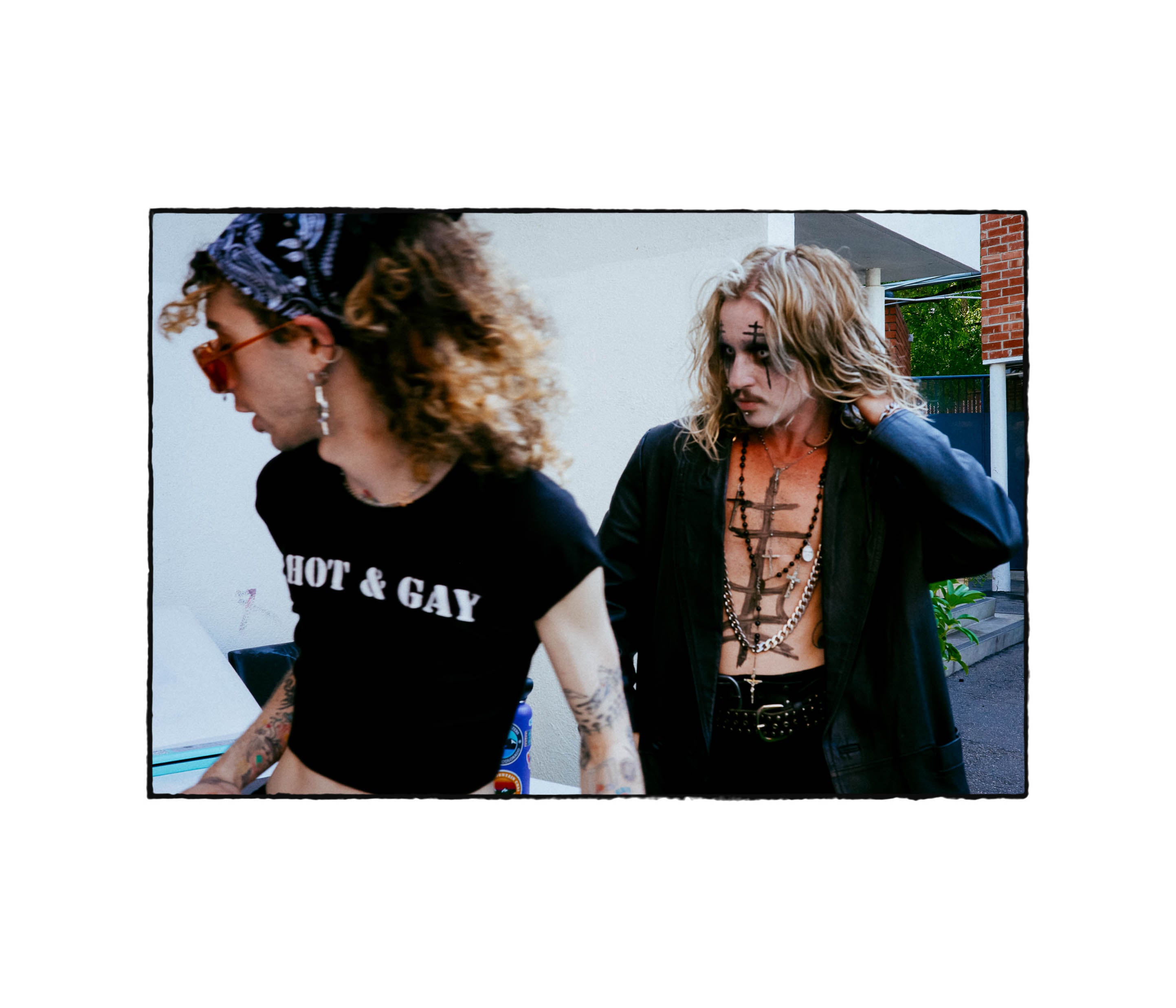 Two people outdoors, one wearing a 'HOT & Gay' shirt, in a casual setting.