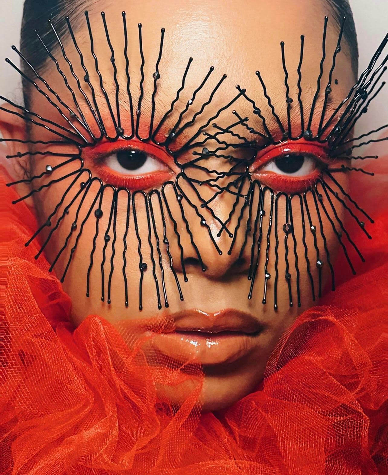 Dee, LA-based makeup artist's photo of a woman with dramatic black spikes radiating from around red rimmed eyes in a red tulle collar.