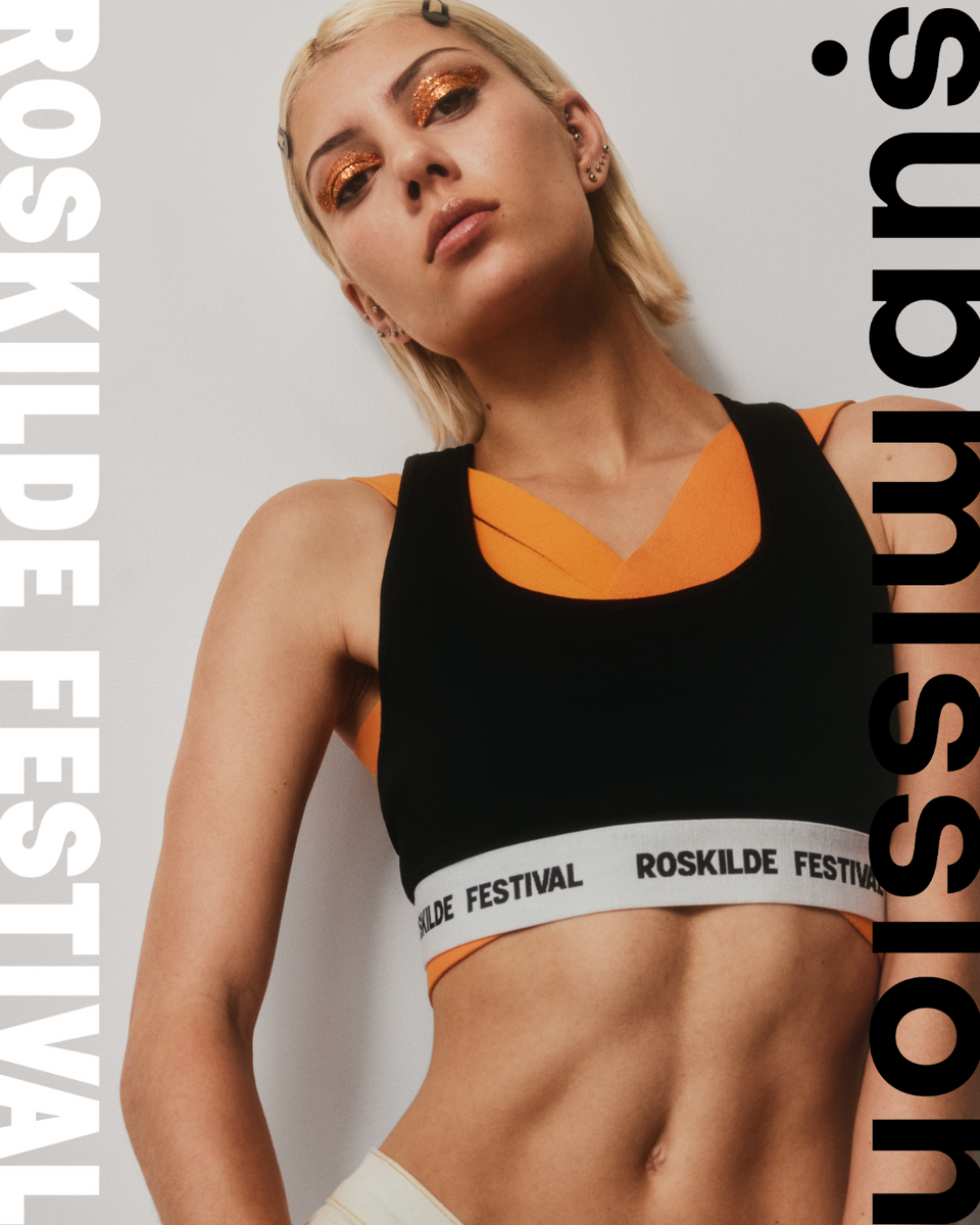 Woman wearing a black and orange sports bra form roskilde festival with visible branding against a plain background and submission beauty orange glitter on her eyes