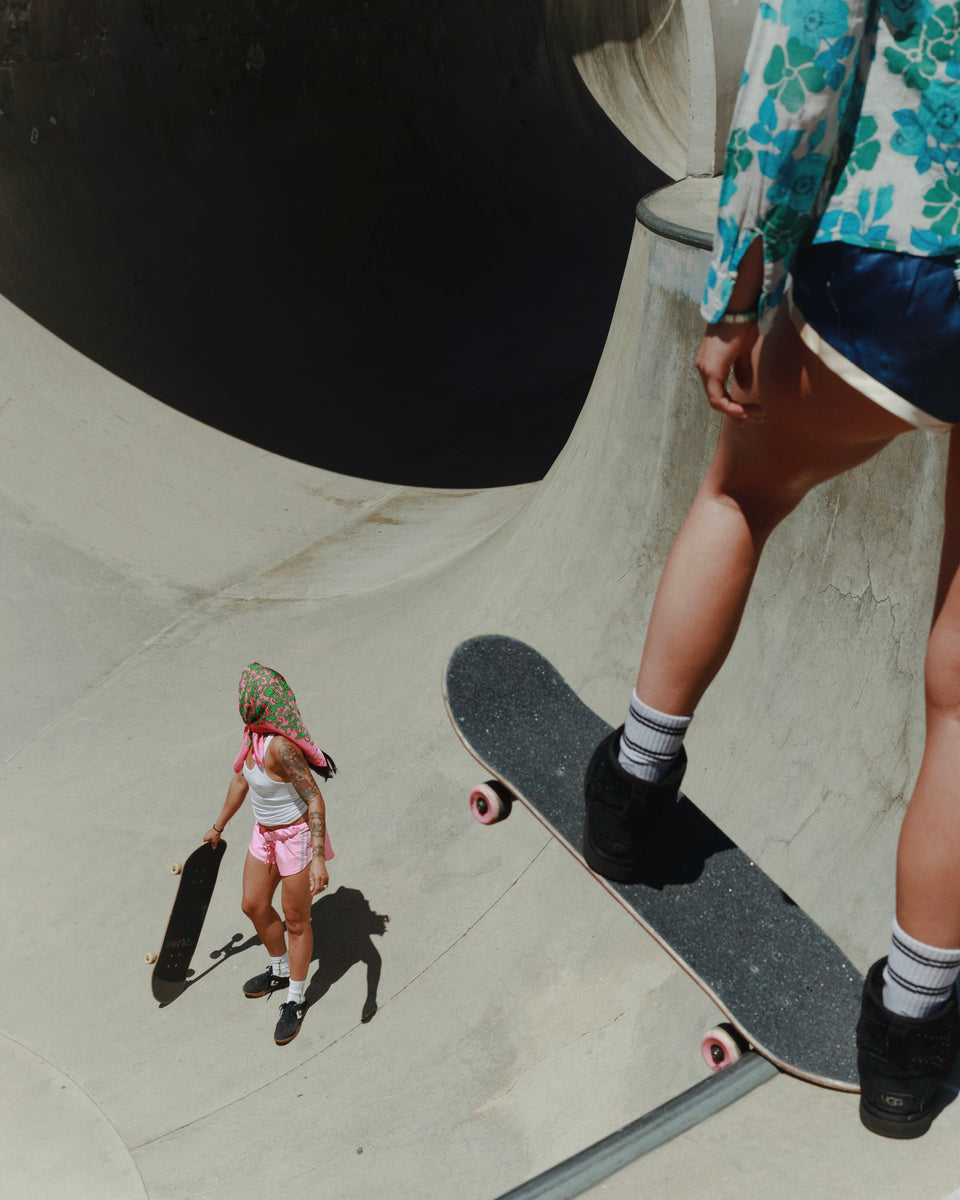 Two people with skateboards at a skate park, one standing on a ramp.