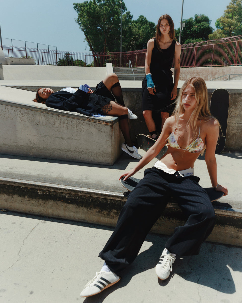 Three people in a skate park setting with one person sitting on a concrete ledge.