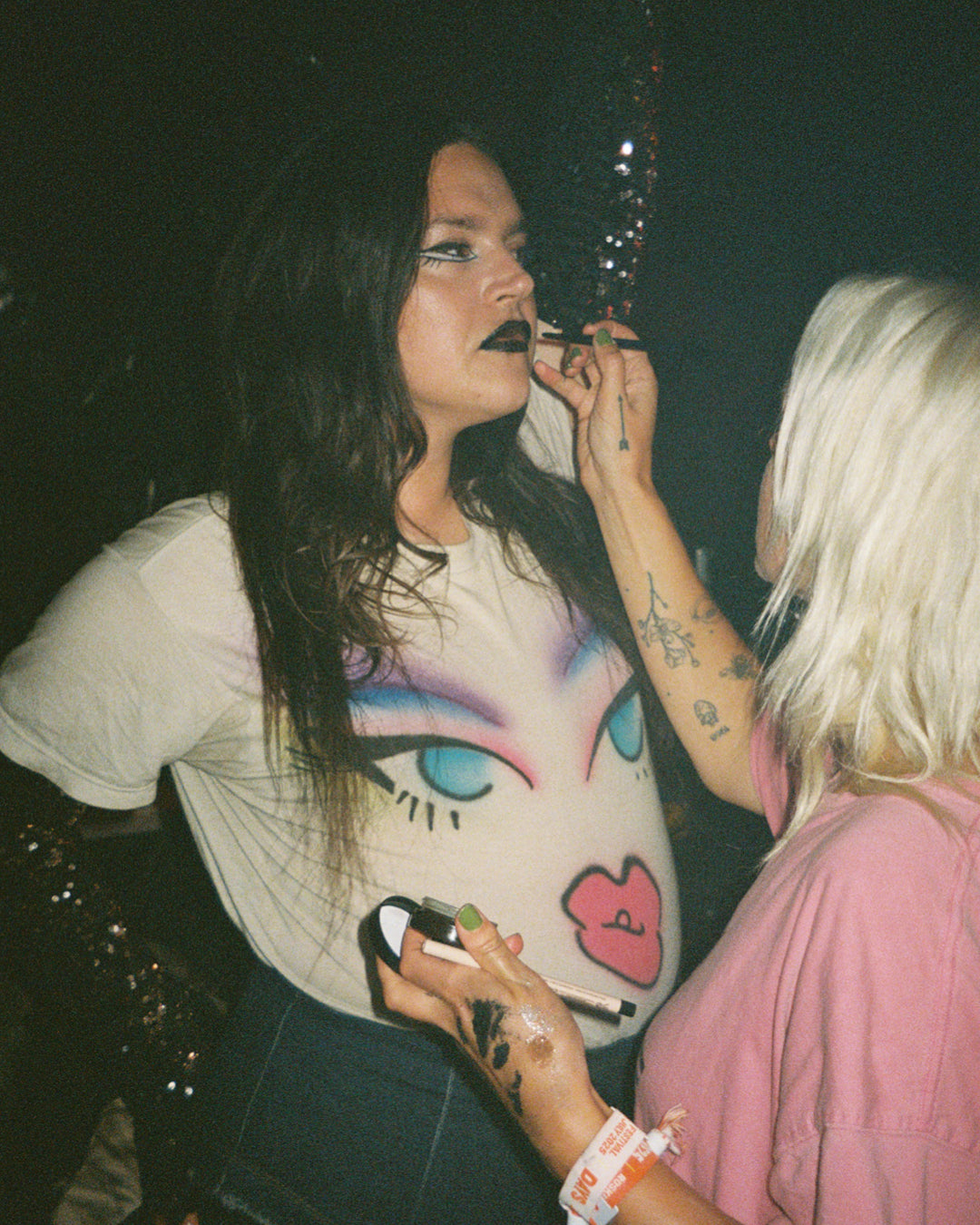 Two women backstage at  djg2g with one applying makeup to the other's face.