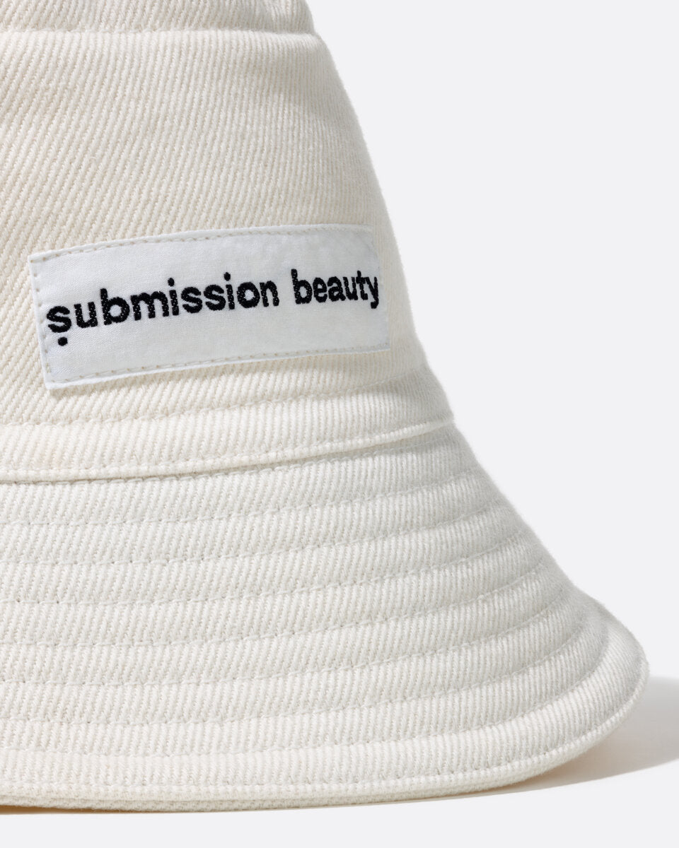 Photo showing  our bucket hat in half profile showing the label reading 'submission beauty', the hat is made of recycled cotton scraps and sustainably sourced cotton