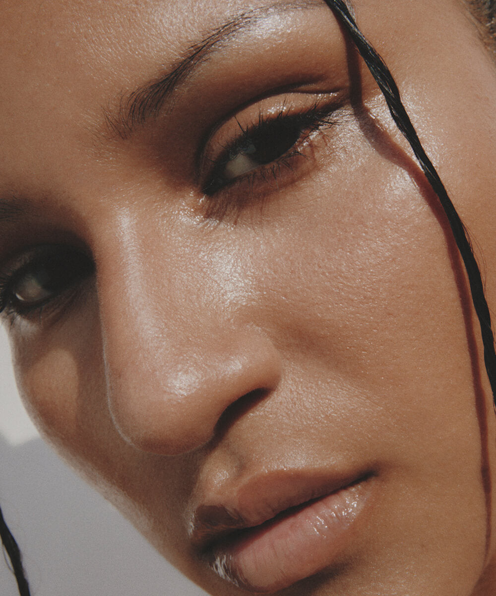 a cropped close-up of the face of a youthful female model  with medium complexion  with  a neutral expression, with Highlighter Light applied to her eyes and lips and face