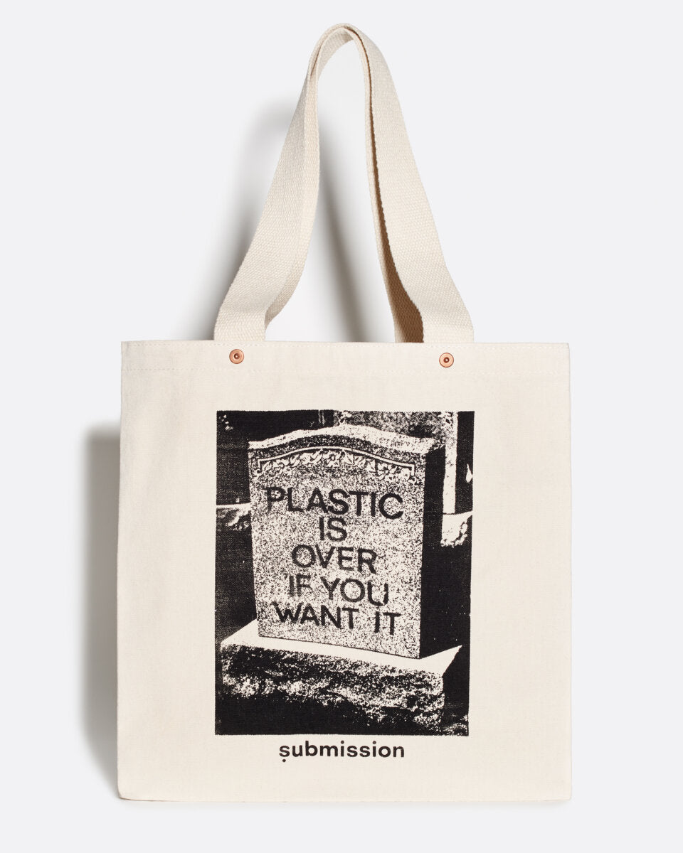 A flat layout product shot   of an off-white tote bag with a large greyscale graphic in the center depicting a headstone with the words “PLASTIC IS OVER IF YOU WANT IT” in capital letters, and two decorative brass snaps