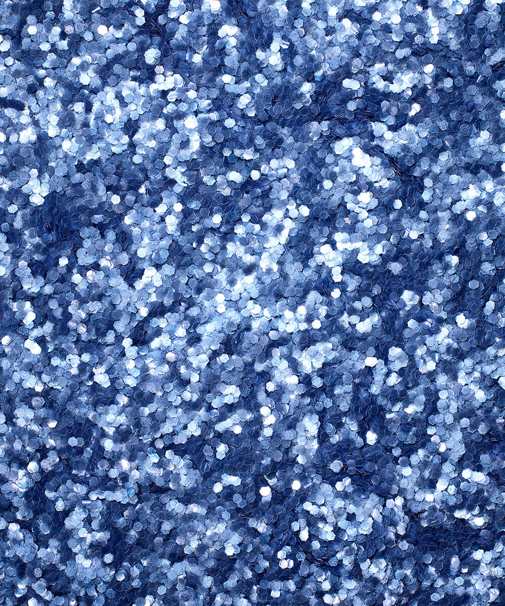 a square, full-bleed overhead view of plastic-free plant-based biodegradable blue glitter flakes highlighting the glitter’s texture and varied shades of blue