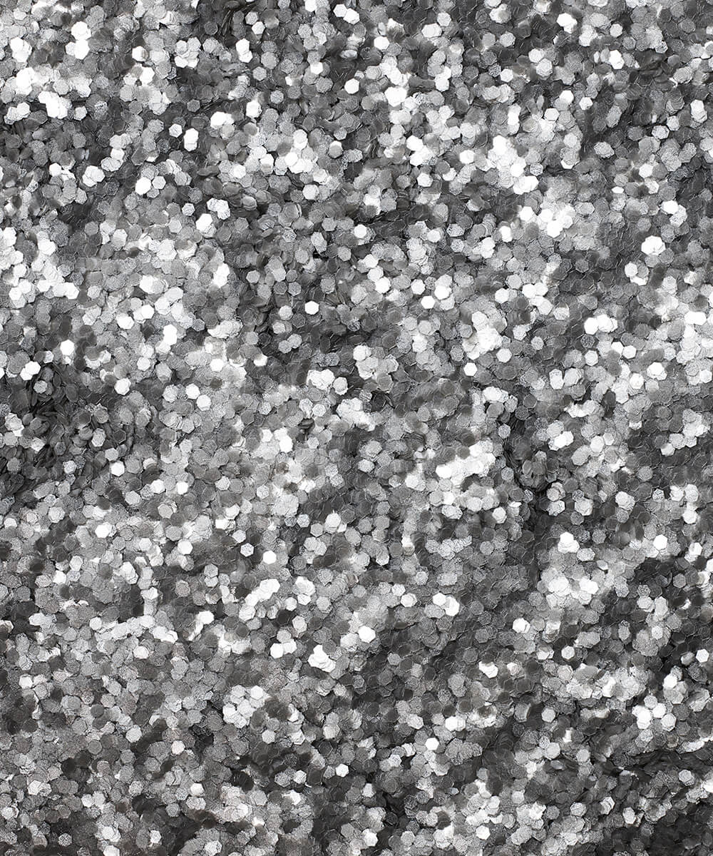 a square, full-bleed overhead view of plastic-free plant-based biodegradable silver glitter flakes highlighting the glitter’s texture and varied shades of silver