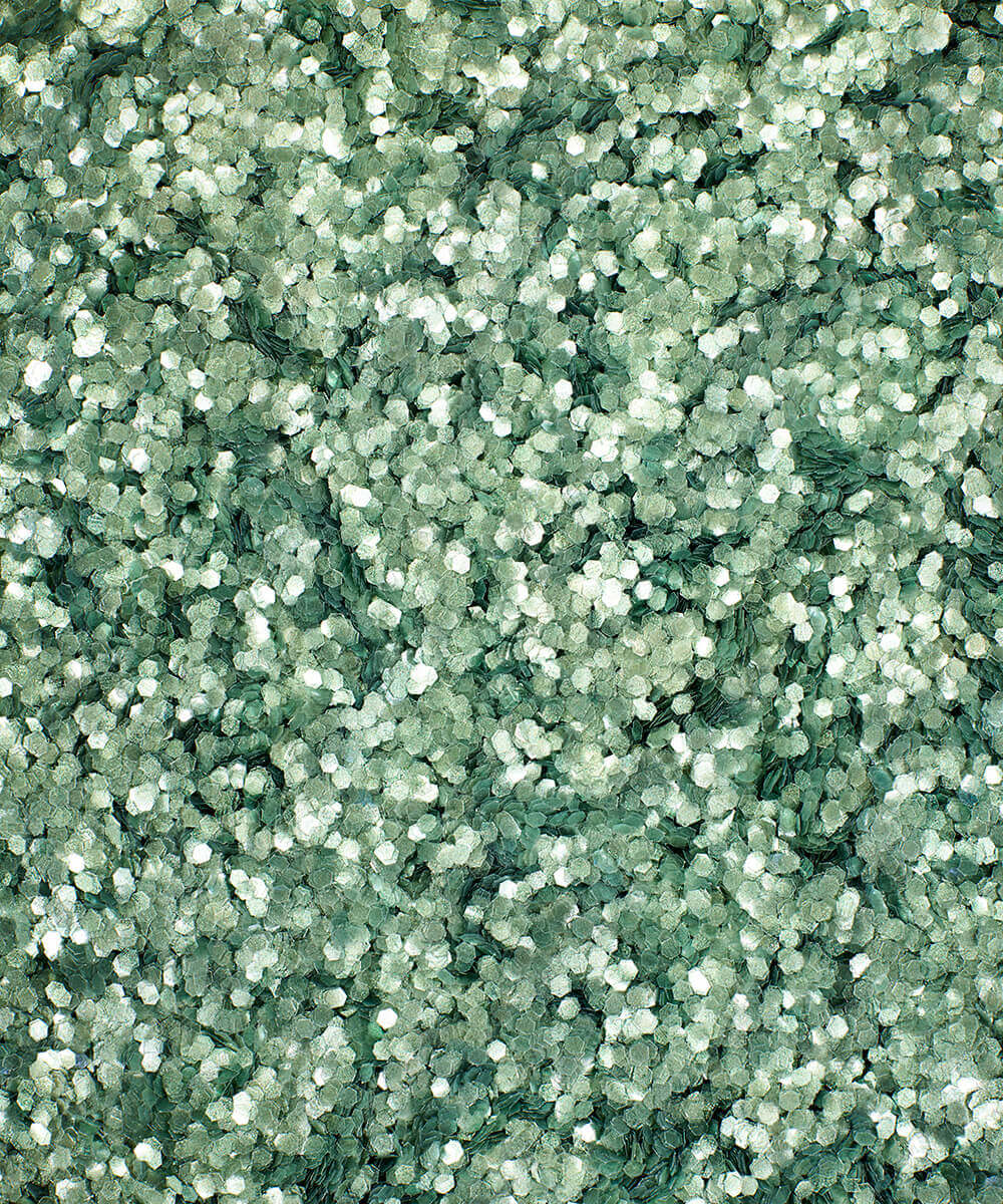 a square, full-bleed overhead view of plastic-free plant-based biodegradable green glitter flakes highlighting the glitter’s texture and varied shades of green